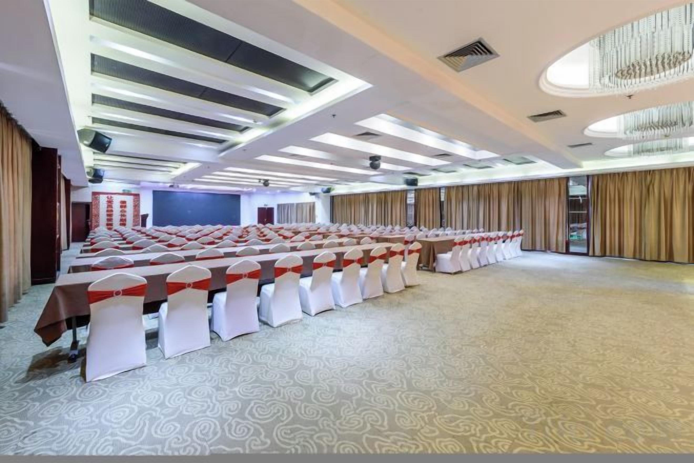 A conference room with long tables, white chairs, and a patterned carpet.