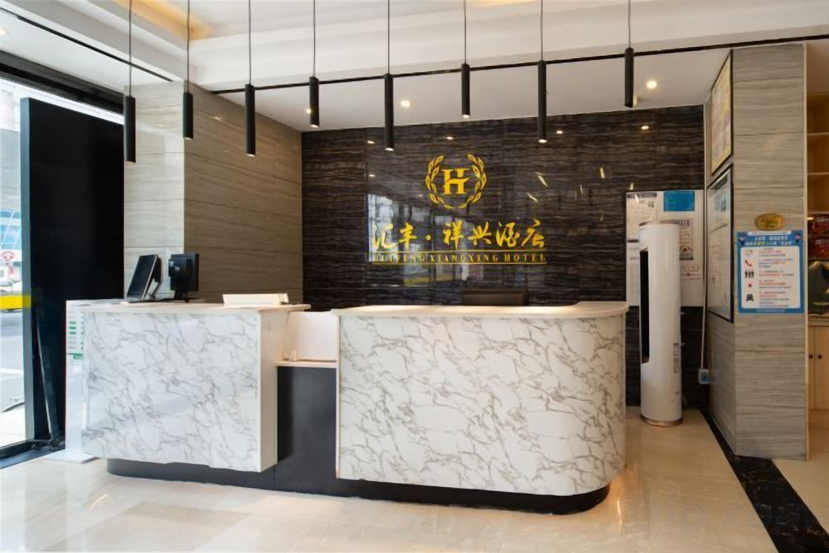 A hotel reception desk with a marble counter, a black wall with gold lettering, and a modern ceiling design.