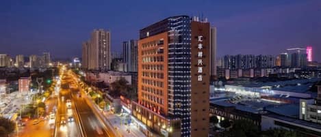 A multi-story hotel with a prominent red facade, located in a cityscape with a busy street in the foreground.