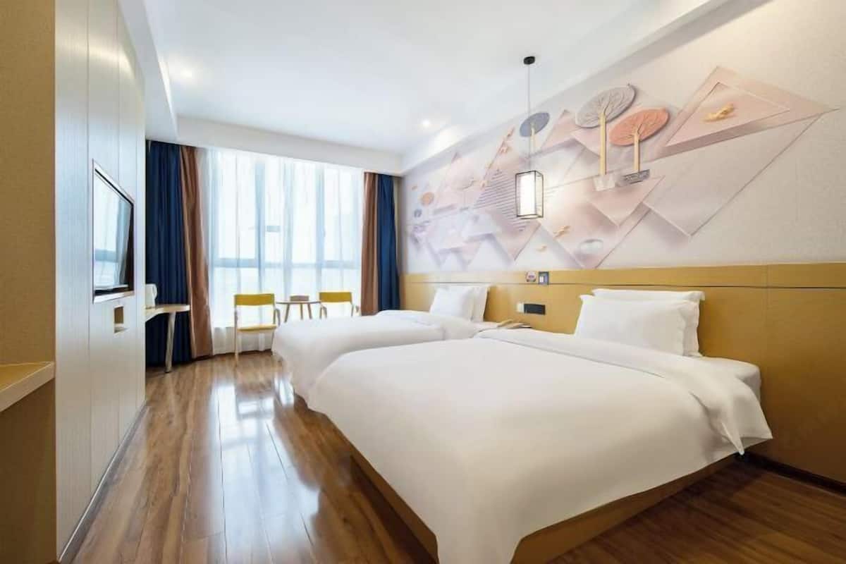 A hotel room with two beds, a TV, a desk, and a large window with curtains.