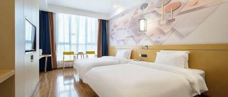 A hotel room with two beds, a TV, a desk, and a large window with curtains.