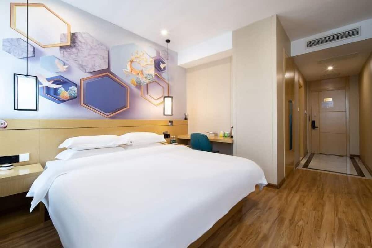 A hotel room with a large bed, a desk, a chair, and a wall with geometric patterns.