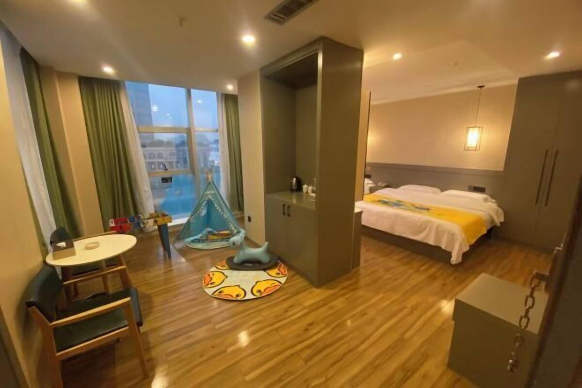 A hotel room with a bed, a desk, a chair, a wardrobe, and a view of the city.