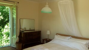 A bedroom with a bed, a dresser, a mirror, a bedside table with a lamp, and a window with a view of greenery. - Peace, Pool and Panoramas in the Monferrato, UNESCO's hidden gem in Italy (Montabone)