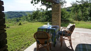 Patio esterno con tavolo e sedie, immerso nel verde e circondato da pareti in pietra.