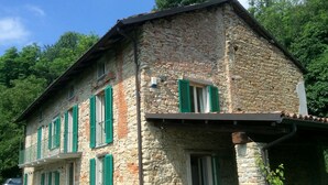 Un edificio in pietra con persiane verdi, un balcone e un tavolo con sedie all'esterno.