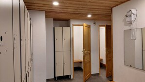 Un pasillo con taquillas, puertas de madera, un banco y un secador de pelo en la pared.