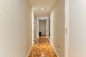 A hallway with a wooden herringbone floor, white walls, and a door at the end. - Feel Porto Syrah Townhouse (Oporto)