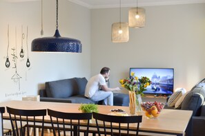 A modern living room with a dining area, a television, and a person sitting on a couch. - Feel Porto Syrah Townhouse (Oporto)