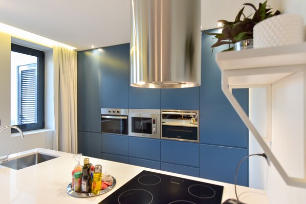 A modern kitchen with blue cabinets, stainless steel appliances, and a central island with a built-in induction cooktop.