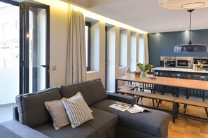 A modern living room with a sofa, a dining table, and a kitchen area.