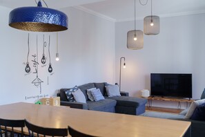 Een moderne woonkamer met een grijze bank, een houten eettafel en een flatscreen televisie.