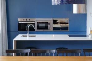 A modern kitchen with built-in appliances, a white countertop, and a dining area with chairs. - Feel Porto Syrah Townhouse (Oporto)