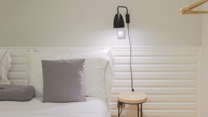 Un lit bien fait, avec des oreillers blancs et gris, une table de chevet avec une lampe et un luminaire fixé au mur.