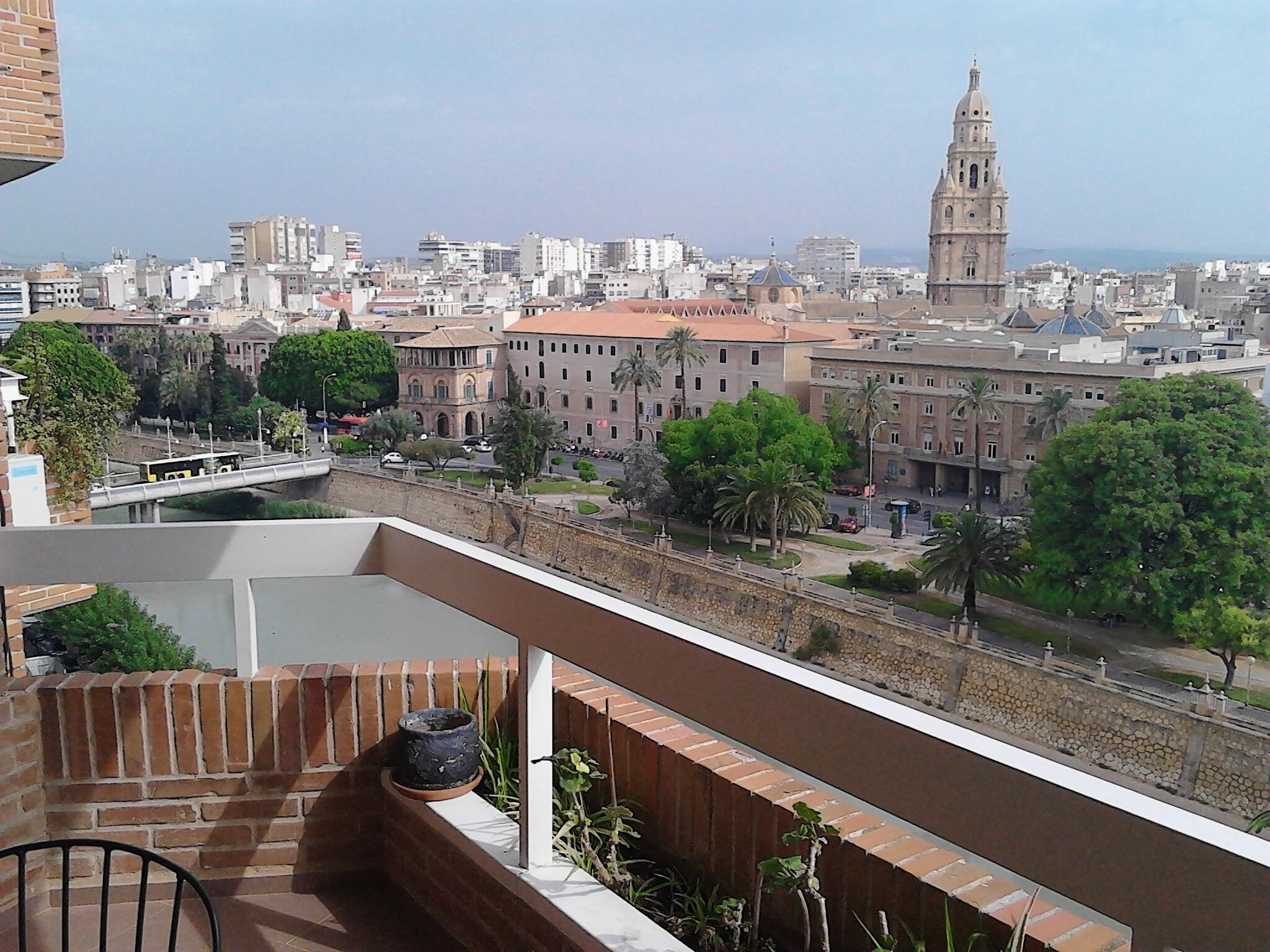 A balcony with a view of a cityscape, including a prominent tower and various buildings.