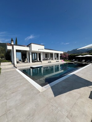 Une maison moderne dotée d’une piscine, d’un espace salon extérieur et offrant une vue sur la montagne.