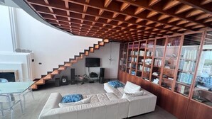 A modern living room with a white sofa, a glass dining table, and a wooden staircase.