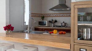 A modern kitchen with a wooden countertop, white stools, a microwave, and a stove.