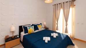 Un lit bien fait, avec une couvre-lit bleue et des serviettes blanches, une lampe de chevet et une table de chevet sur laquelle se trouvent un téléphone et un objet décoratif.