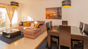 Un salon moderne avec un canapé, une table basse et une table à manger avec des chaises. Il y a un tableau au mur et une fenêtre avec des rideaux.