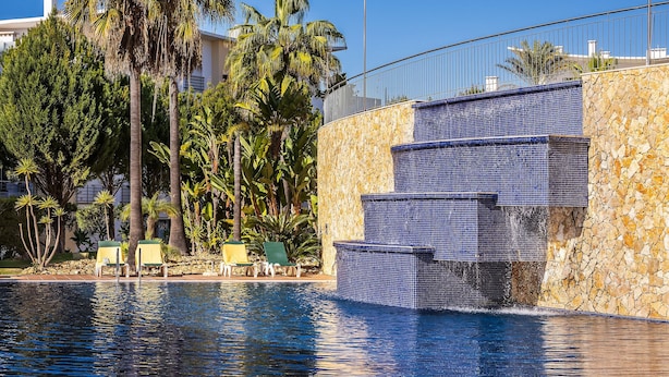 Une piscine à l’eau d’un bleu cristallin, entourée de palmiers et de chaises longues.