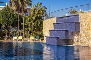 Une piscine à l’eau d’un bleu cristallin, entourée de palmiers et de chaises longues.