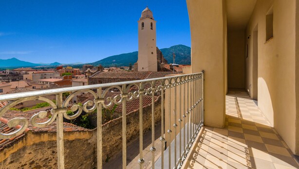 A balcony with a metal railing overlooking a cityscape with a prominent tower and mountains in the distance.