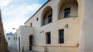 A narrow street with a building featuring arched windows and a balcony.