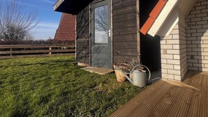 A small wooden shed with a door, a step leading up to it, and a potted plant beside it. - Detached holiday home for 6 people with garden near the Wadden Sea & beach (Den Oever)