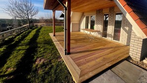 A covered patio with a wooden deck, a brick wall, and a window. - Detached holiday home for 6 people with garden near the Wadden Sea & beach (Den Oever)