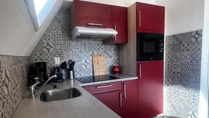 A kitchen with a stainless steel sink, red cabinets, a microwave, and patterned backsplash tiles. - Detached holiday home for 6 people with garden near the Wadden Sea & beach (Den Oever)