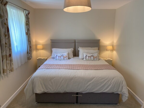 A bedroom with a bed, two bedside tables, a lamp, and a window with curtains.