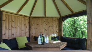 Un belvédère en bois avec une table dressée pour prendre un verre, entouré de sièges confortables.