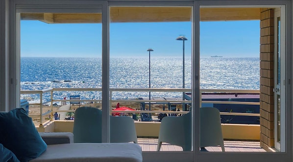 A balcony with a view of the ocean, a chair, and a table.