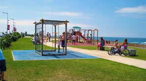 A playground with a climbing structure and slides, surrounded by a grassy area and a walking path.
