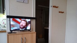 A television on a wooden cabinet in a room with a door leading to a bathroom. - rent pretty calm and pleasant studio (Bagnoles De L'orne Normandie)