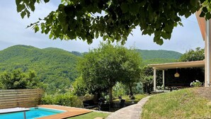 Un patio trasero con piscina, un deck de madera y un sendero de piedra que lleva a una zona de estar cubierta.