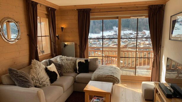 A cozy living room with a sofa, a small table, and a view of a snowy landscape through large windows.