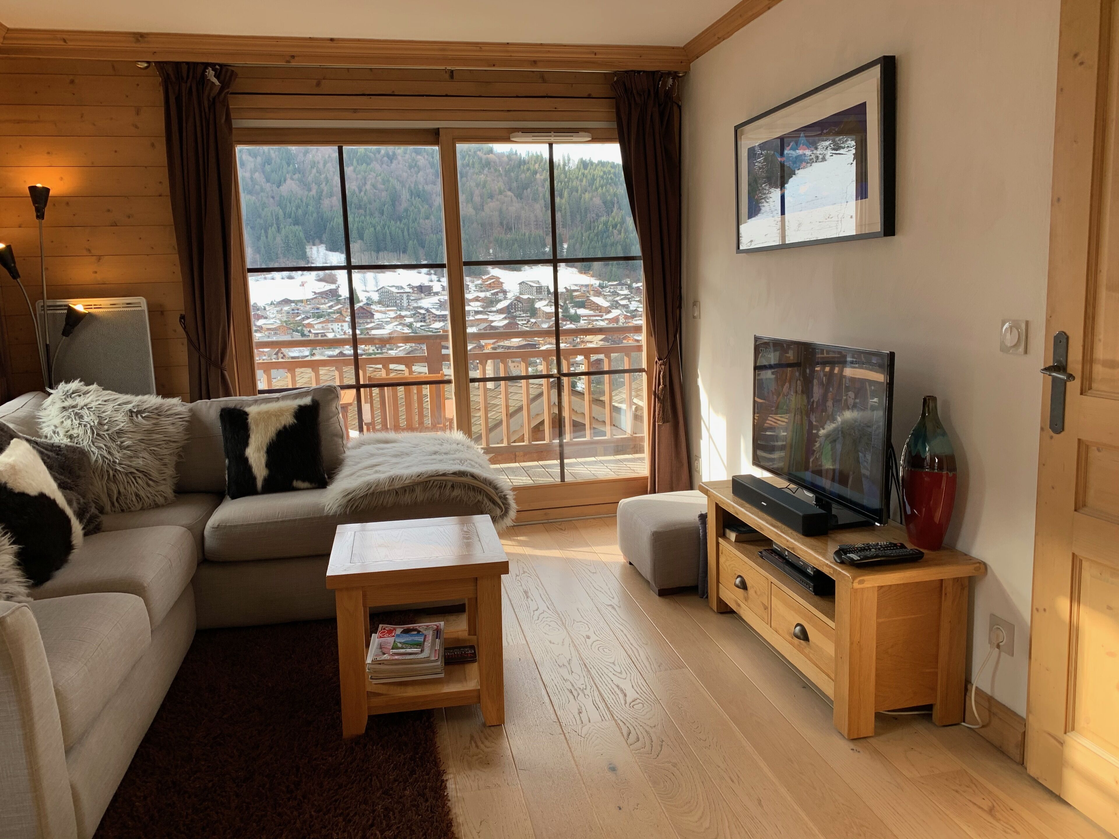 A cozy living room with a sofa, a coffee table, a TV, and a view of a snowy landscape through large windows.