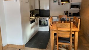 A compact kitchen with white cabinets, a wooden dining table, and a black tiled floor.