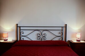 A bed with a metal headboard, two bedside tables with lamps, and a red bedspread.