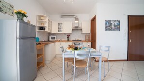 A compact kitchen with a refrigerator, microwave, stove, and a dining table with chairs. There is a small shelf unit and a door with a picture on the wall. - Comfort and brightness in Lucca (Lucca)