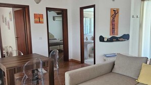 A living room with a sofa, a dining table with chairs, a wooden ceiling, and artwork on the walls. - Villa surrounded by greenery with private pool  (Palazzolo Acreide)