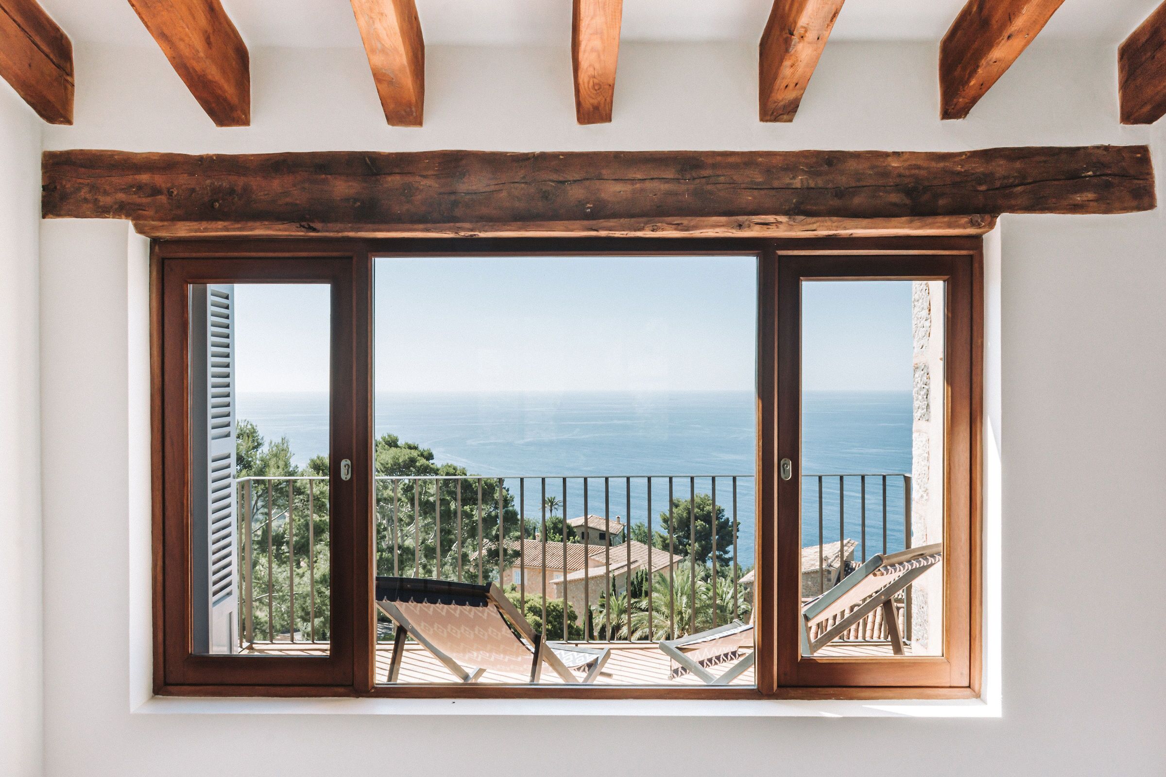 Ein Zimmer mit großem Fenster und Blick auf eine Küstenlandschaft, mit Holzboden und Meerblick.