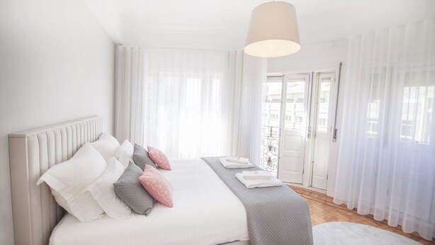 Ein Schlafzimmer mit einem großen Bett, weißen Vorhängen, einer Pendelleuchte und Blick nach draußen.