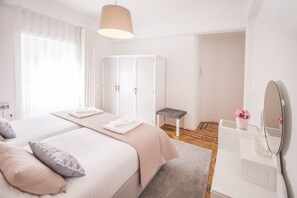 A modern bedroom with a large bed, a wardrobe, a vanity with a mirror, and a small stool. - Apartment for families & friends (Porto)
