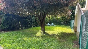 A grassy outdoor area with a tree, a fence, and two white lounge chairs. - Rural Accommodations Casa Fabián, La Tenada (Pet Friendly) (Castrillón)
