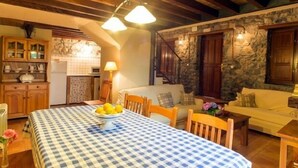 A cozy room with a checkered tablecloth, wooden furniture, a stone wall, and a kitchen area with cabinets and a refrigerator. - Rural Accommodations Casa Fabián, La Tenada (Pet Friendly) (Castrillón)