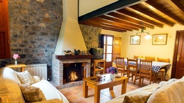 A cozy living room with a stone wall, a fireplace, wooden furniture, and a dining area. - Rural Accommodations Casa Fabián, La Tenada (Pet Friendly) (Castrillón)