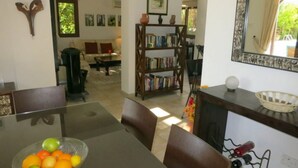 A dining area with a glass table, chairs, and a bowl of fruit. There is a bookshelf with books and a mirror on the wall. - Luxury Villa With Private Pool, Landscaped Garden And Sea Views (Pissouri Bay)